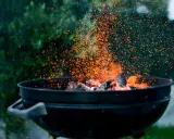 Un barbecue en plein air, avec des braises incandescentes et des étincelles qui dansent. L'odeur du barbecue bois ou charbon emplit l'air.