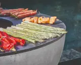 Légumes et brochettes de poulet sur un brasero, prêts pour une recette estivale. Carottes, poivrons rouges, asperges et poulet grillé.