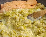Filets de saumon poêlés sur une fondue de poireaux crémeuse, parsemée d'herbes. Une cuillère en bois remue ce plat savoureux.