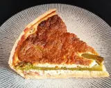 Tranche de tarte aux asperges blanches, garnie d'une préparation crémeuse et dorée, sur une assiette texturée.