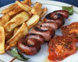 Assiette de saucisse à la plancha, frites dorées et tomates grillées. Un délice estival !