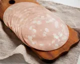 Tranches de mortadelle cuit ou cru, disposées en éventail sur une planche à découper en bois, sur un tissu de lin.