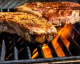 Deux entrecôtes savoureuses en cuisson sur un barbecue, les flammes dansent sous la viande.