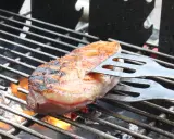 Magret de canard en cuisson indirecte sur un Weber, retourné avec une spatule. La peau est grillée et dorée, la chair rosée.