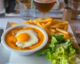 Un plat savoureux avec un œuf au plat sur une sauce orangée, des frites dorées et une salade verte. Un vrai délice, on se demande d'où vient le welsh !