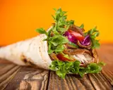 Un délicieux kebab maison garni de viande, salade croquante, tomates et chou rouge, sur un fond orange vif.