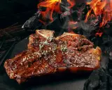 Un steak T-bone juteux, garni de thym, cuit sur des braises ardentes. Une parfaite recette barbecue pour les amateurs de viande.
