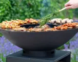 Un brasero moderne cuit brochettes et saucisses. On y voit comment fonctionne un brasero, avec une branche de romarin pour parfumer.