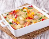 Un gratin de légumes coloré et crémeux, avec des poivrons, courgettes et autres légumes dans une sauce onctueuse, prêt à être dégusté.