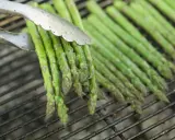 Des asperges vertes grillées, parfaites pour une recette simple et savoureuse. Les pinces saisissent un bouquet prêt à être retourné.