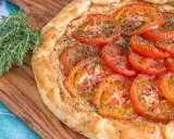 Une délicieuse tarte tomates aux herbes, sur une planche en bois, avec une branche de thym frais à côté.
