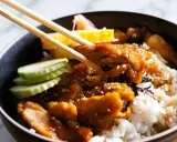 Un bol de riz garni de poulet teriyaki, de concombre, d'omelette et de gingembre mariné, prêt à être dégusté avec des baguettes.