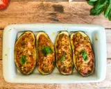 Quatre moitiés d'aubergines garnies de légumes et de fromage gratiné, décorées de feuilles de basilic frais.