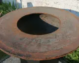 Gros plan sur le plateau rouillé d'un brasero, prêt pour son culottage. La surface métallique présente des nuances orangées et grises.