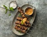 Brochettes d'agneau grillées au barbecue, servies avec une sauce aux arachides et garnies de menthe fraîche.