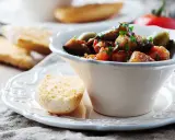 Un bol de caponata sicilienne, plat sicilien aux aubergines, tomates et olives, garni de persil frais. Servi avec du pain grillé.