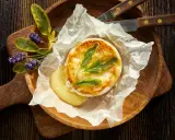 Camembert au barbecue, fondant et doré, servi sur papier sulfurisé avec des herbes aromatiques et des fleurs de lavande. Un délice à partager.