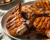 Trois côtes de porc barbecue, grillées et nappées d'une sauce savoureuse, sur une assiette blanche.