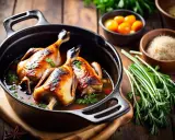Deux cuisses de canard dorées mijotent dans un jus savoureux, accompagnées de tomates cerises et de romarin frais. Un plat appétissant.