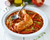 Un plat de poulet basquaise savoureux, avec un morceau de poulet doré dans une sauce tomate riche aux poivrons rouges et verts, garni de persil frais.