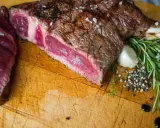 Un succulent côte de bœuf barbecue, saignant et parsemé de gros sel, est prêt à être dégusté. Accompagné de romarin frais, d'ail et de poivre concassé.