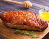 Un magret de canard au barbecue, la peau dorée et croustillante, servi sur une planche en bois avec du thym frais et une sauce au miel.