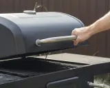 Main d'homme ouvrant le couvercle d'un barbecue noir. Apprenez comment utiliser un barbecue avec couvercle pour des grillades parfaites.