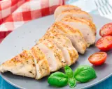 Un délicieux filet de poulet grillé, tranché et servi avec des tomates cerises et du basilic frais sur une assiette grise.