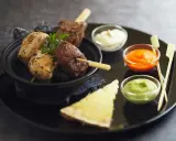 Brochettes de poulet et de bœuf, accompagnées de différentes sauces : mayonnaise, sauce tomate épicée et sauce verte.