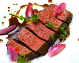 Une succulente entrecôte de bœuf, tranchée et nappée d'une sauce riche, accompagnée de jeunes pousses et d'oignons rouges marinés.