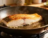 Un filet de morue grillée dore dans une poêle, sa peau croustillante et sa chair nacrée. La vapeur s'échappe, promettant un délice savoureux.