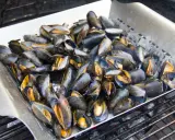 Un plateau de moules au barbecue, prêtes à être dégustées. Les coquilles sombres et orangées s'entrouvrent sous la chaleur des braises.