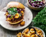 Un délicieux burger de pulled pork garni de fruits et de persil frais, accompagné d'une salade de chou rouge et de fruits confits.