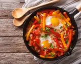 Poêlée de poivrons, tomates et œufs, une recette de piperade savoureuse, garnie de persil frais.