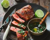 Un steak de bœuf juteux, tranché et garni d'une sauce pour viande de bœuf fraîche et vibrante, accompagné de quartiers de citron vert.