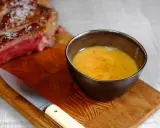 Un bol de sauce pour côte de bœuf, onctueuse et dorée, à côté d'une côte de bœuf saignante et d'un couteau sur une planche en bois.