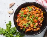 Un bol de chili sin carne, garni de persil frais, avec des haricots rouges, du maïs et des poivrons. Parfait pour un repas réconfortant.