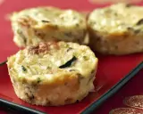 Trois petits flans de courgettes dorés et appétissants sur une assiette rouge, parfaits pour un repas léger.