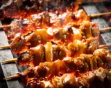 Brochettes de bœuf et fromage grillées sur des braises ardentes, dégageant une fumée alléchante.