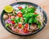 Un bol de soupe pho savoureux avec du bœuf, des boulettes, des nouilles, des herbes fraîches, des piments et un quartier de citron vert.