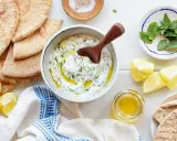 Un bol de tzatziki crémeux, garni d'aneth et d'huile d'olive, prêt à être dégusté avec du pain pita. Une recette fraîche et savoureuse.