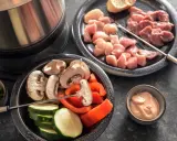 Préparation d'une fondue bourguignonne 3 viandes : cubes de poulet et bœuf crus, champignons, courgettes, poivrons et sauce.