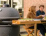 Un couple profite d'un repas en plein air avec une pizza fraîchement préparée, la cuisson kamado promettant une saveur incomparable.
