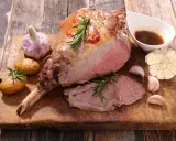Gigot d'agneau rôti, servi avec des pommes de terre, de l'ail et une sauce. Une recette gastronomique qui met l'eau à la bouche.