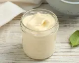 Un pot de mayonnaise sans huile, crémeuse et onctueuse, sur une table en bois. Une feuille verte à côté.