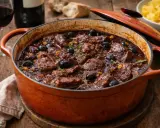 Un plat mijoté de daube de boeuf, garni d'olives noires et de thym, dans une cocotte en fonte orange.