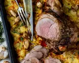 Un gigot d'agneau rôti, tranché, servi sur un lit de pommes de terre gratinées avec de l'ail et du romarin.