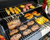 Côtelettes d'agneau, brochettes de légumes et pommes de terre sur un barbecue. La température du barbecue est parfaite pour une cuisson savoureuse.