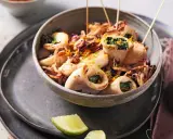 Calamars à la plancha farcis aux herbes, servis dans un bol avec des zestes d'orange et des quartiers de citron vert.