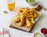 Un plat de fish and chips croustillant, servi avec des frites dorées, un quartier de citron, et des sauces. Une bière blonde complète ce repas.